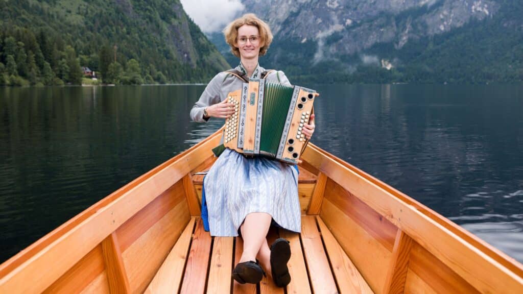 Das Ergebnis von "Harmonika richtig üben": Celia spielt entspannt und lächelnd ihre Steirische Harmonika in einem Boot auf einem Bergsee.
