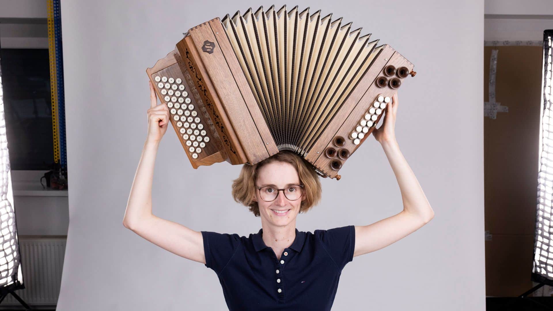 Celia hebt ihre Steirische Harmonika mit beiden Händen über den Kopf, was den Erfolg beim Harmonikalernen einfängt